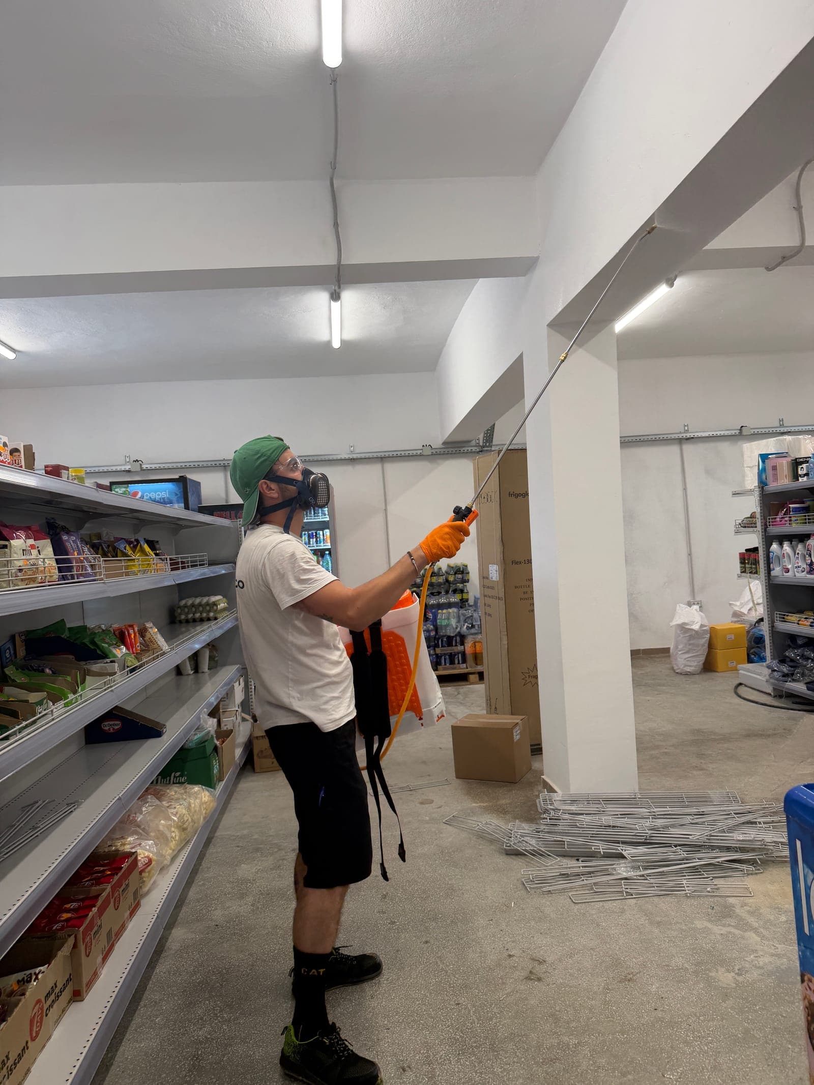 Tehnician Orynco cu semimască de protecție și pulverizator cu lance, aplicând tratament de dezinsecție în zona de tavan a unui magazin alimentar din Oradea